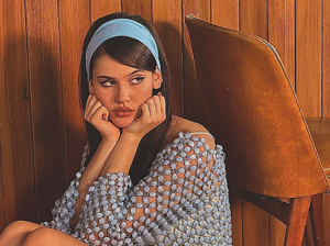 Sienna Spiro sitting against wood panel wall wearing blue headband