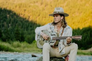 JJ Julius Son of KALEO playing guitar outdoors during A/B anniversary era