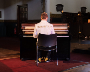 John Galea playing piano during Songwriter music video performance in church setting