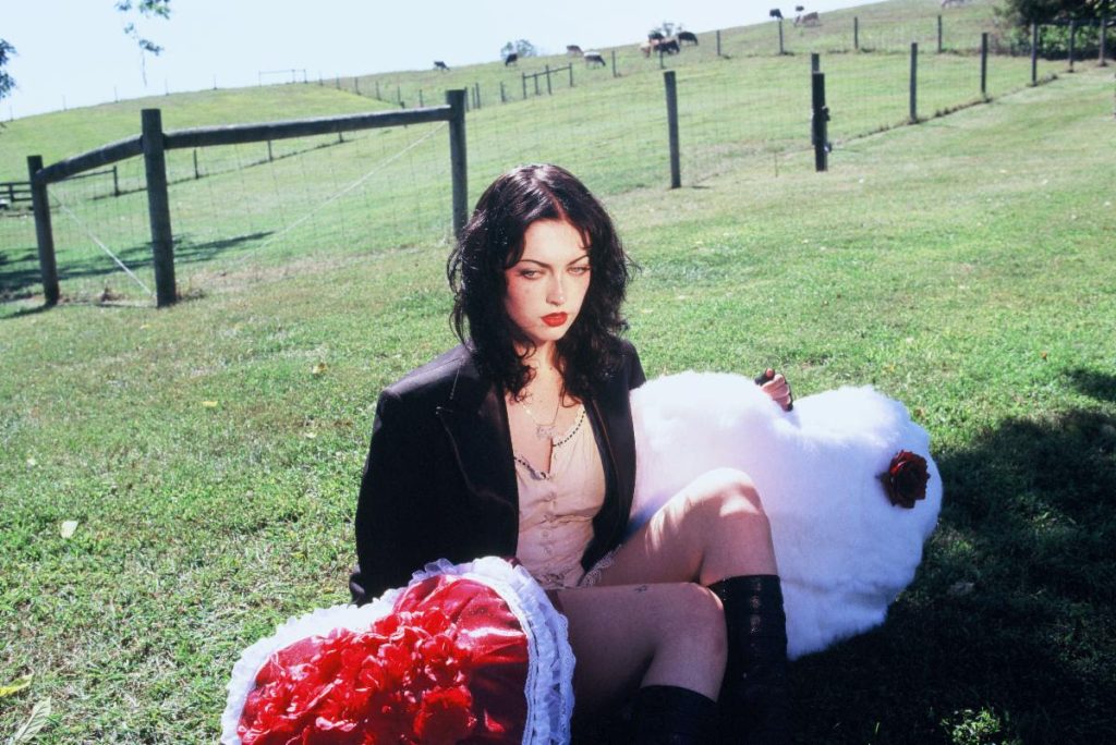 Violet Grohl sitting in field holding heart props Cool Buzz single Be Sweet To Me album era