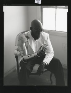 BNYX® poses in black and white portrait wearing a white blazer and futuristic robotic arm during the GENESIS FM album campaign.
