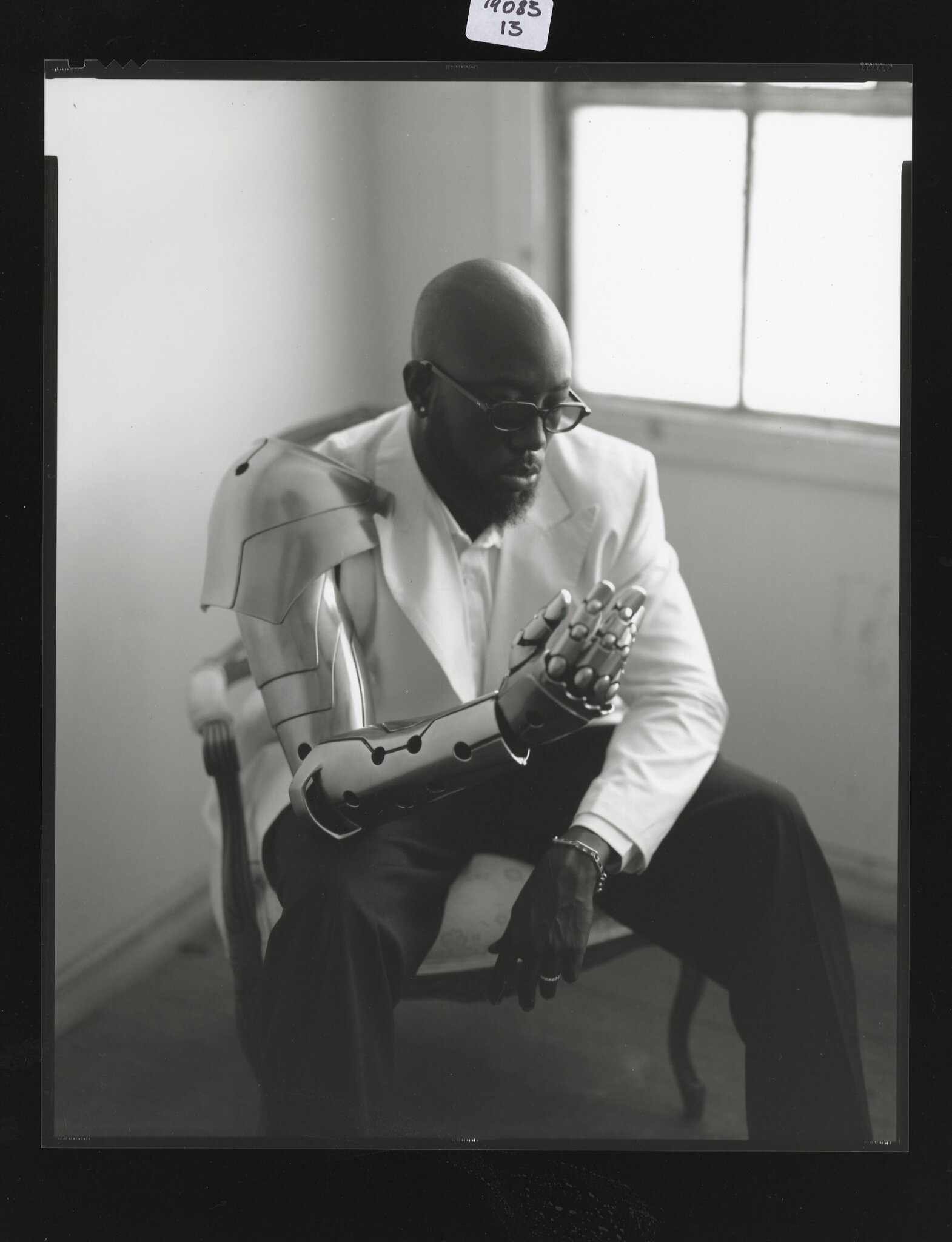 BNYX® poses in black and white portrait wearing a white blazer and futuristic robotic arm during the GENESIS FM album campaign.