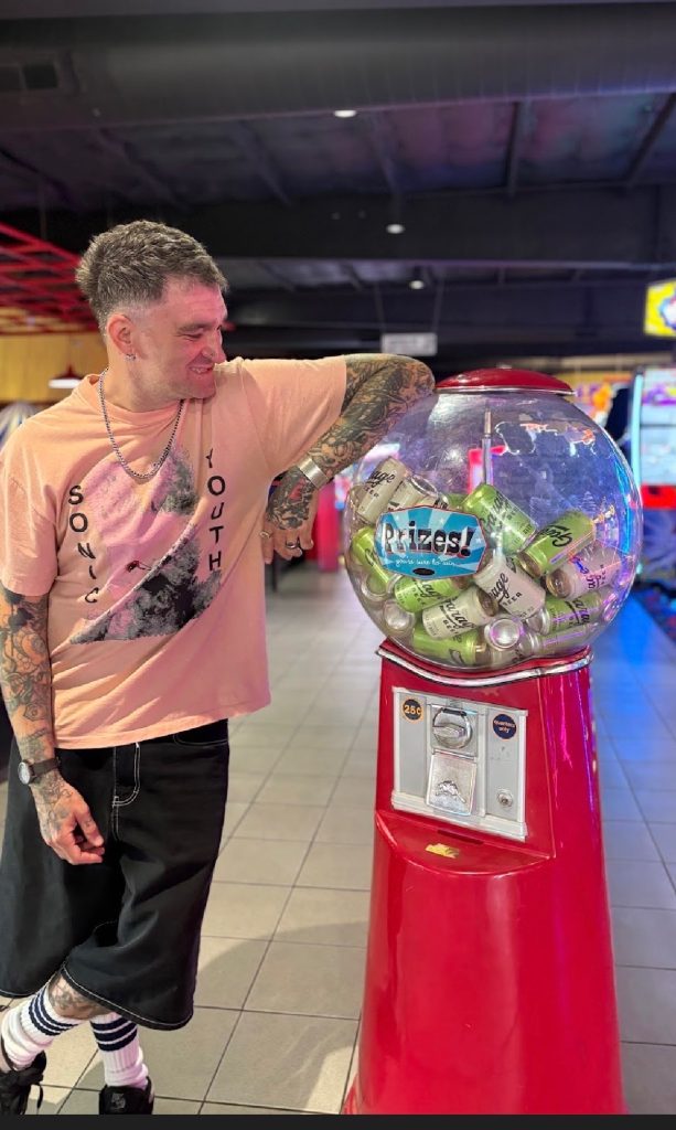 Jordan Pundik standing beside vintage gumball machine filled with Garage Beer cans inside arcade
