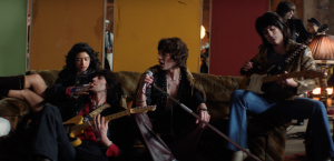 Actors portraying a young 1970s-era Rolling Stones perform and relax on a vintage couch in a scene from the “In The Stars” music video.