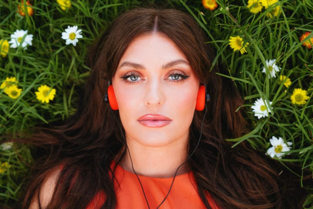 Janine portrait lying in flowers with headphones promoting Pain and Paradise Deluxe
