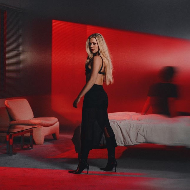 Becky Hill standing in red-lit room wearing black outfit for Hands On Me single visual