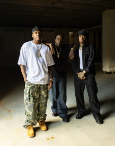 Clipse members Pusha T and Malice pose with rapper J.I.D in an industrial warehouse setting ahead of their 2026 Red Rocks Amphitheatre concert announcement.