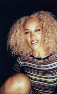 Jorja Smith appears in promotional artwork for her single "What’s Done Is Done," featuring handwritten neon-style lettering and a candid black-and-white portrait.