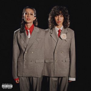 Towa Bird appears in mirrored tailoring on the cover of her 2026 album Gentleman, standing beside a duplicate version of herself in matching gray suits and red ties.