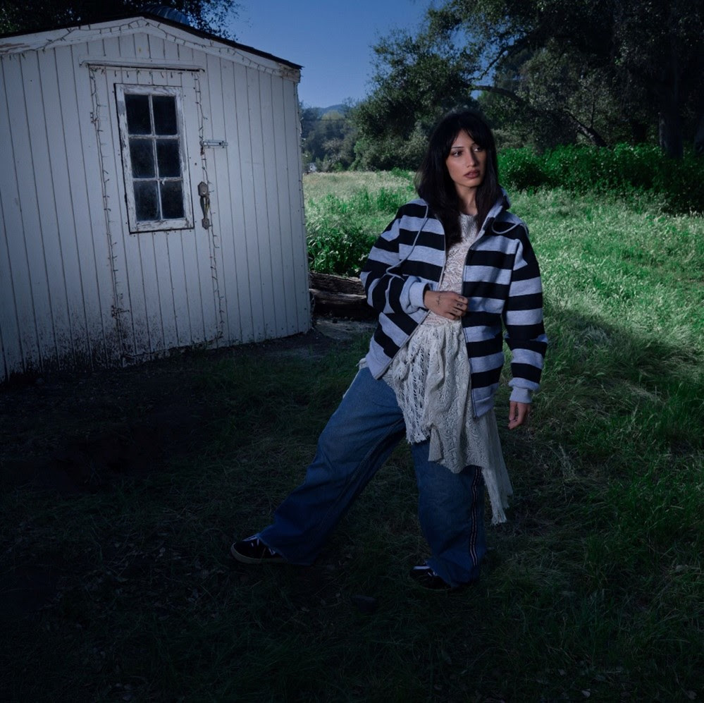 Leyla Ebrahimi sitting by a creek in a wooded outdoor setting wearing a white tee and black pants