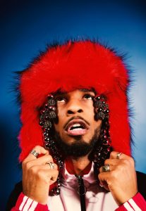 Armani White wearing a bright red fur hat with beaded details during a stylized portrait shoot for “[PRESS]”