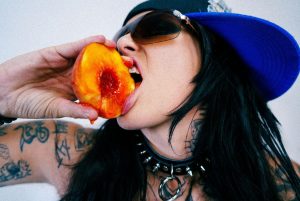 Lauren Sanderson biting peach in edgy promotional image for COME SAY SUM remix