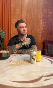 New Found Glory vocalist Jordan Pundik sitting at table with Garage Beer, cereal, and tattooed arms visible