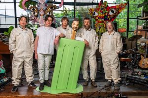 Modest Mouse band members pose in matching jumpsuits inside a colorful studio space ahead of the release of An Eraser and A Maze