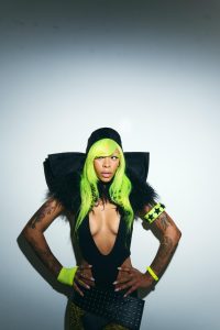 Rico Nasty poses in a black bodysuit with neon green hair and matching accessories against a white backdrop