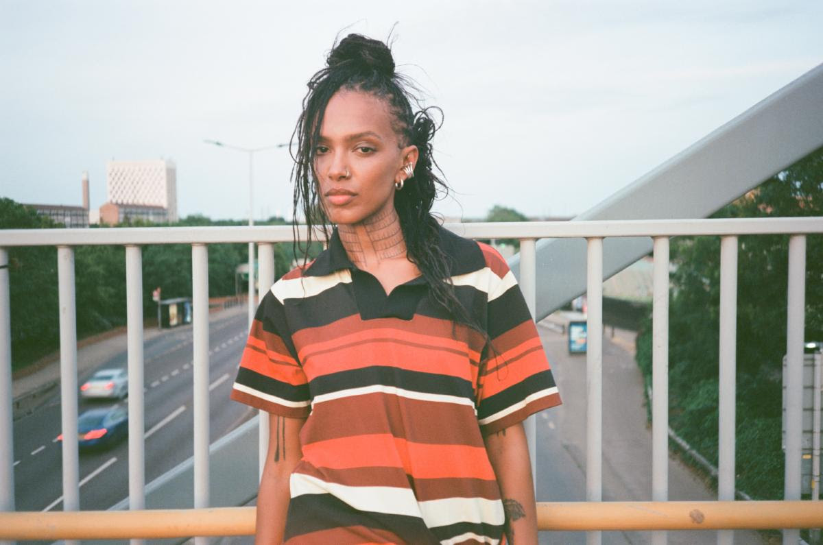 Alewya stands on an overpass in London wearing a striped shirt, showcasing her distinctive visual style ahead of the release of ZERO