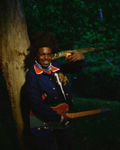 Kodak Black poses with a guitar in a wooded setting while promoting his surprise 2026 mixtape Kodak The Blessing.