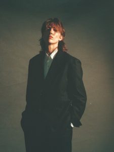 E.R. Fightmaster poses in an oversized black suit and white shirt in a moody portrait promoting the debut album Tolerance