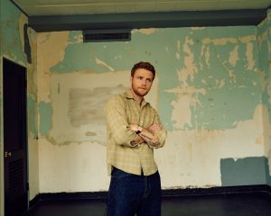 Alex Warren standing in a weathered room promoting his upcoming album WILDCHILD