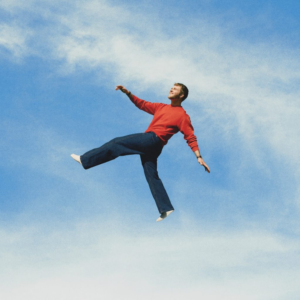 Alex Warren suspended against a blue sky during promotional campaign for WILDCHILD album
