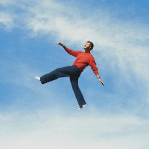 Alex Warren suspended against a blue sky during promotional campaign for WILDCHILD album