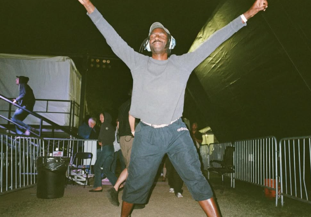 Blood Orange, also known as Dev Hynes, celebrates backstage with his arms raised during a live performance event.