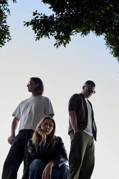 Jungle band members Josh Lloyd-Watson, Tom McFarland, and Lydia Kitto pose outdoors ahead of the release of their 2026 album Sunshine.