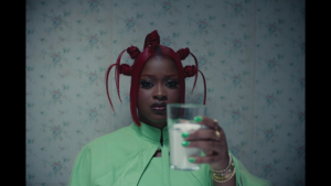 Tierra Whack holds a glass of milk in a scene from the "CANDLE WAX" music video from her mixtape WHACK'S MUSEUM.