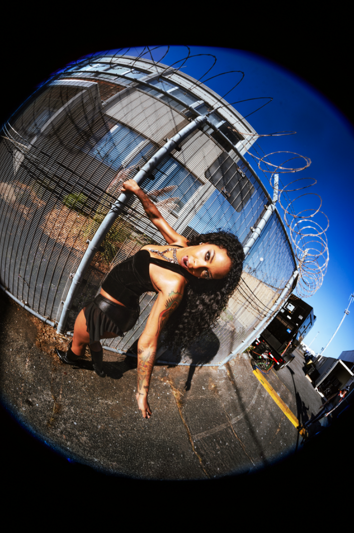 Rico Nasty poses beside a chain-link fence in a promotional photo for her 2026 album RX
