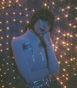 Karen O poses beneath sparkling lights in a promotional portrait for her collaboration with The Avalanches on "Blue Shadows."