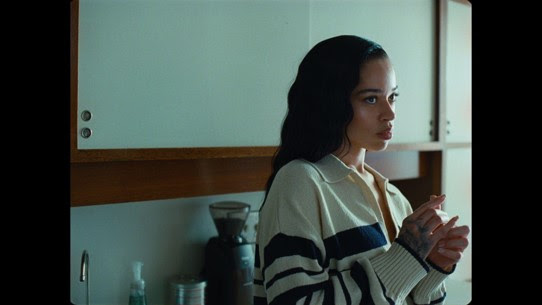Ella Mai stands thoughtfully in a kitchen during a scene from the "Might Just" music video.