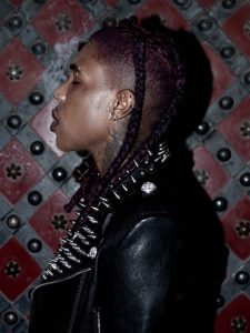 Destroy Lonely in profile wearing a black spiked leather jacket with purple braids.