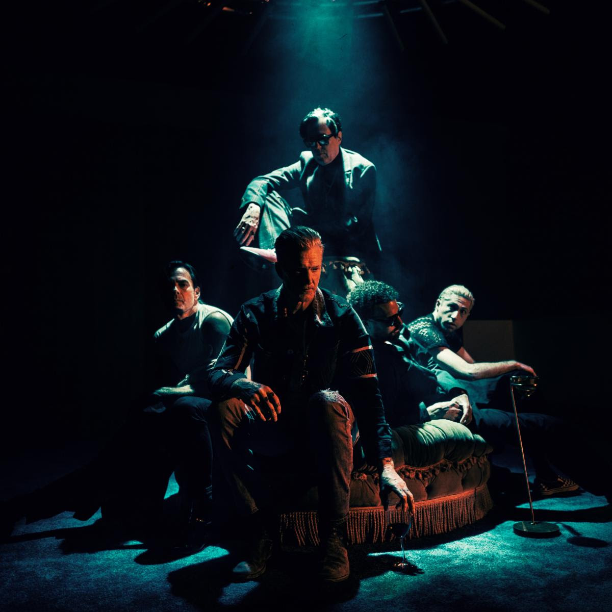 Queens of the Stone Age posed together in a dark room under dramatic teal lighting.