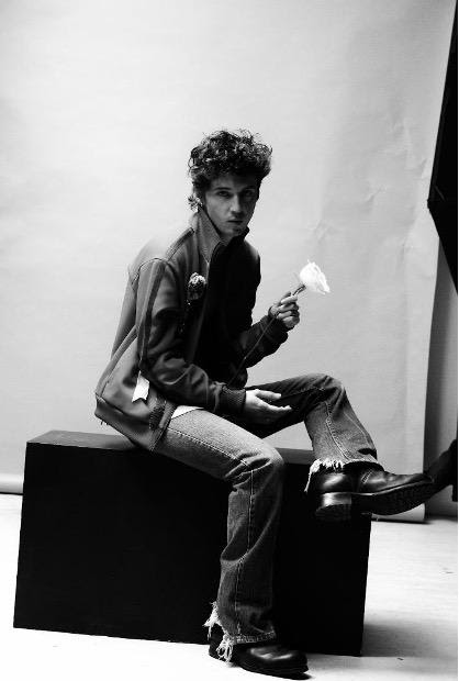 Marcus Cooper seated in a black-and-white studio portrait holding a white flower.