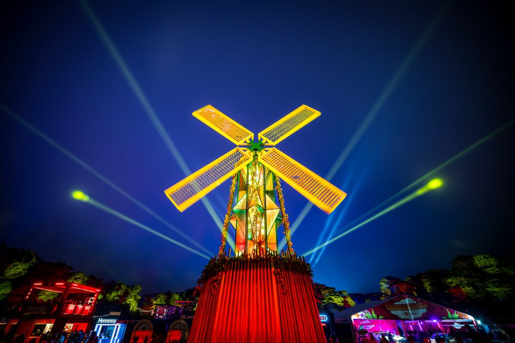 The illuminated Outside Lands windmill glows beneath colorful beams of light at night in Golden Gate Park.