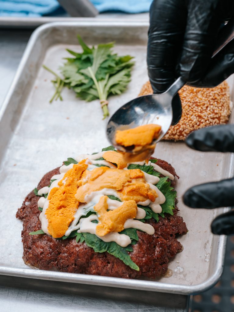 Uni being added to a burger with greens and sauce at Outside Lands 2026.