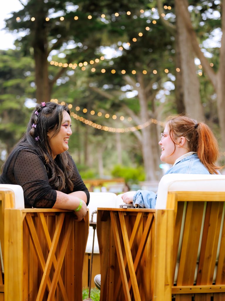 Two Outside Lands 2026 festivalgoers talking at a seating area beneath string lights in Golden Gate Park.