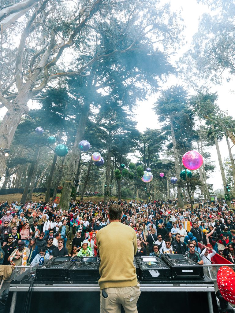 A DJ performs for a packed crowd beneath colorful hanging disco balls at the Duboce Triangle stage during Outside Lands 2026.