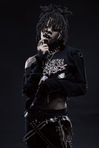Novulent photographed in black clothing and layered chains against a dark background