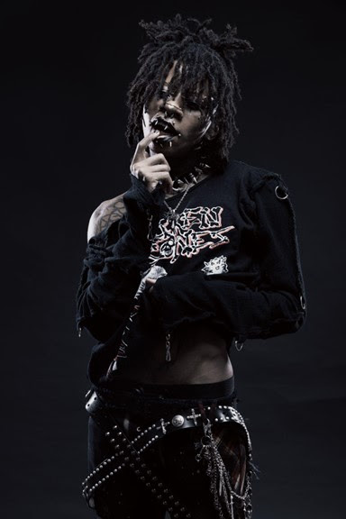 Novulent photographed in black clothing and layered chains against a dark background