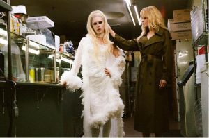 Phoenix Johnson in a glamorous white feathered look beside Nicole Kidman in a backstage setting.
