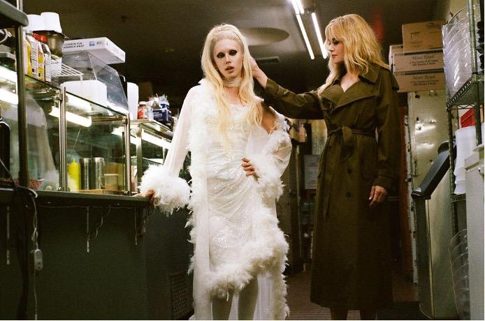 Phoenix Johnson in a glamorous white feathered look beside Nicole Kidman in a backstage setting.