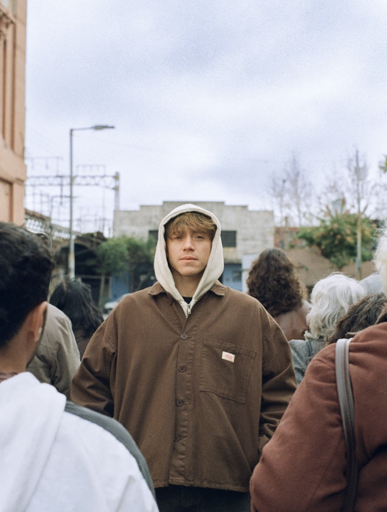 Paulo Londra outdoors in a brown jacket and gray hoodie during his 2026 era