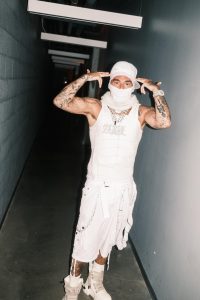 eat wearing an all-white outfit, face covering and cap during his 2026 COCOON era