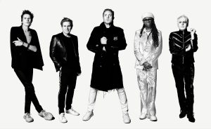 Black-and-white promotional portrait of Duran Duran members John Taylor, Roger Taylor, Simon Le Bon and Nick Rhodes alongside Nile Rodgers, standing against a white background.