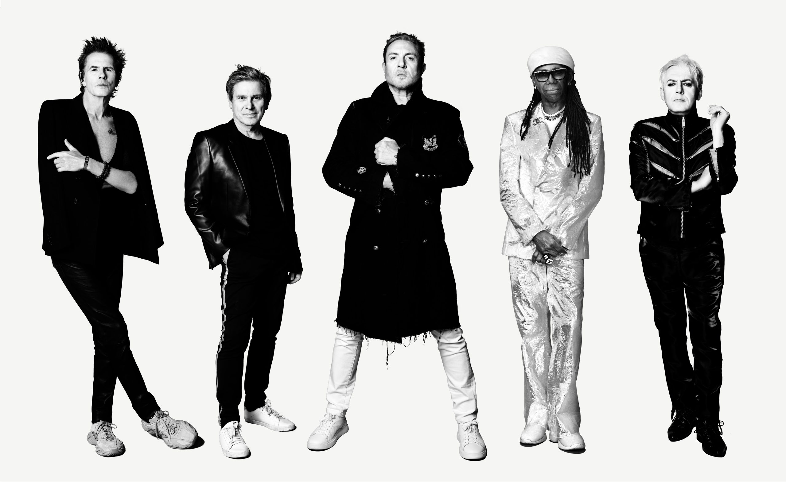 Black-and-white promotional portrait of Duran Duran members John Taylor, Roger Taylor, Simon Le Bon and Nick Rhodes alongside Nile Rodgers, standing against a white background.