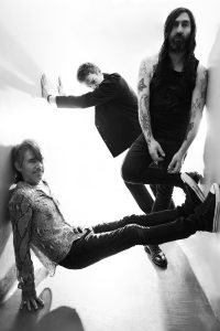 Black-and-white promotional portrait of the three members of Princess Goes posing in a narrow white corridor.