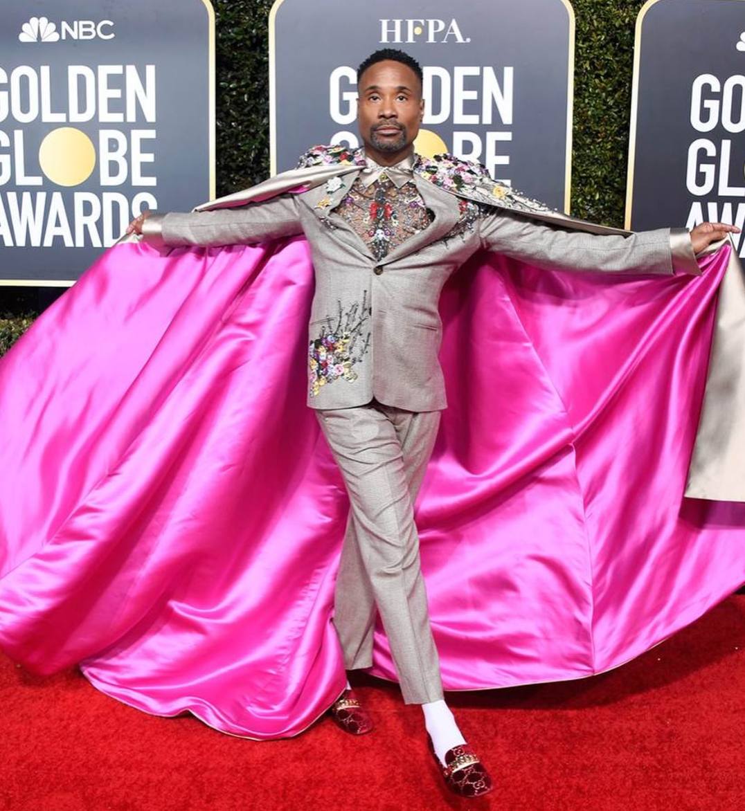 Billy Porter poses on the Golden Globes red carpet wearing a gray embroidered suit with a dramatic hot pink satin cape.