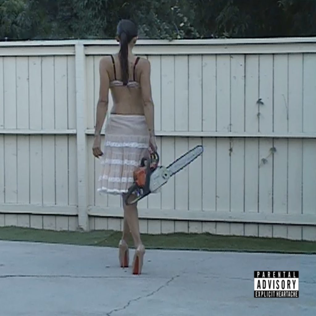 A woman photographed from behind wearing platform heels and a sheer skirt while carrying a chainsaw beside a white fence, with an Explicit Heartache advisory label.